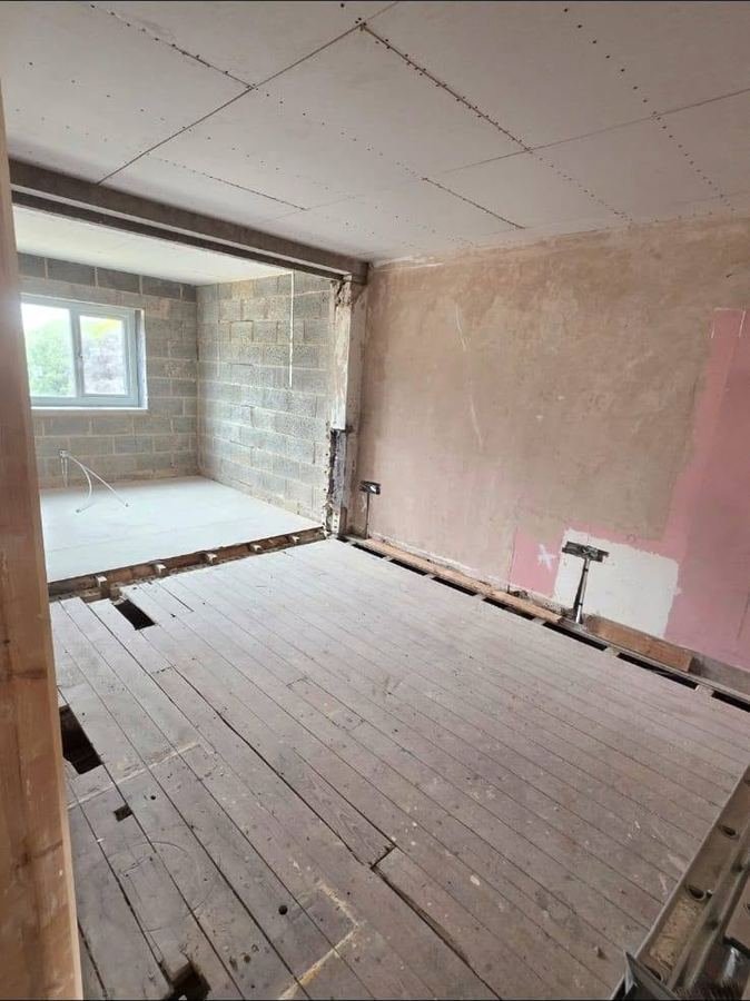 A room stripped back to bare blockwork and floor joists, with a new opening cut through