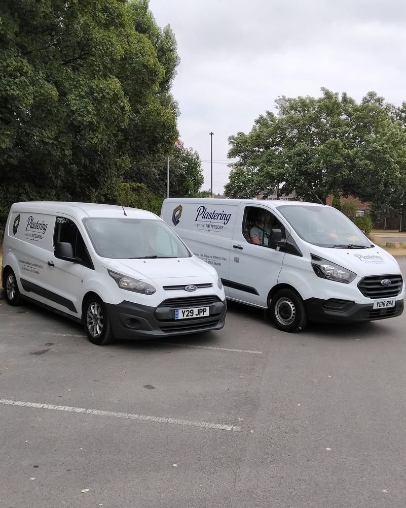 The two Plastering by the Pattersons vans, signwritten with the business name and phone numbers